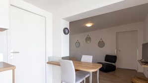 Un espace repas moderne avec une table en bois, des chaises blanches, une chaise noire et un téléviseur posé sur un meuble.