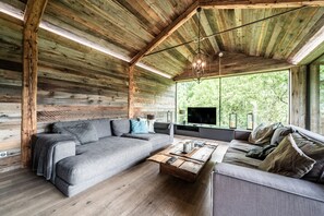 Interno di una baita di legno con un divano grigio, un tavolino in legno e un televisore.