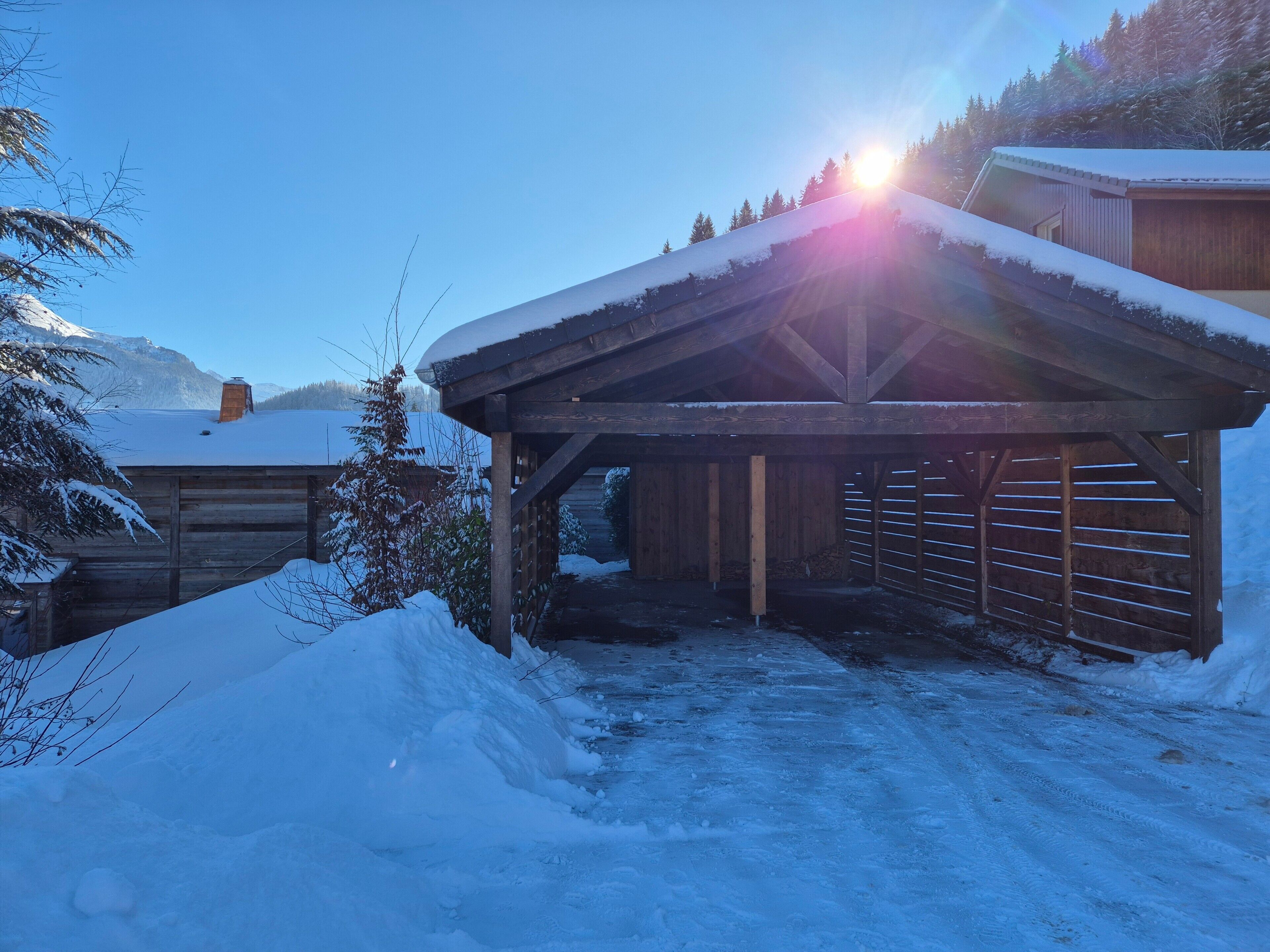 A wooden building with a sloped roof, surrounded by snow-covered ground and trees.