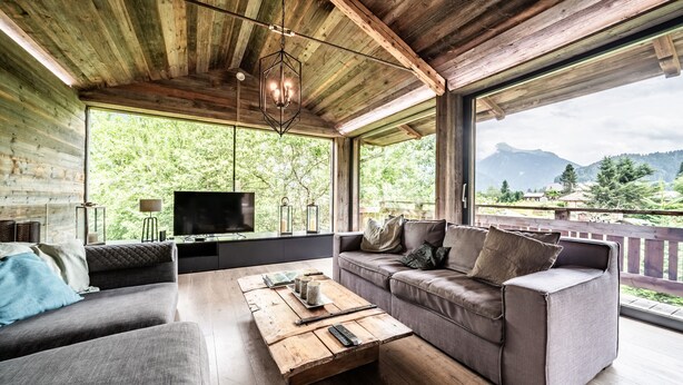 A modern log cabin interior with a large window, a sofa, a coffee table, and a television.