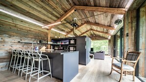 A rustic kitchen with wooden walls, a bar area with stools, and a large window.