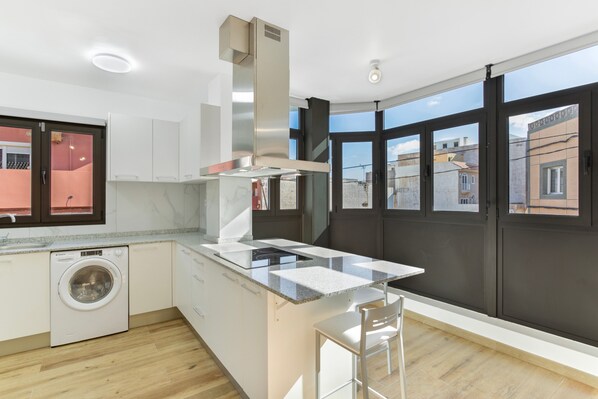 A modern kitchen with a built-in washing machine, a stainless steel range hood, and large windows offering views of the city.