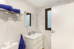Un baño con lavamanos blanco, espejo y perchero.