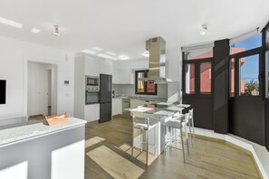 Una cocina moderna con armarios blancos, una campana extractora de acero inoxidable y un horno empotrado.