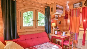 L’intérieur d’un chalet en bois comprend un lit, une table avec des chaises, une fenêtre avec des rideaux et un tableau accroché au mur.