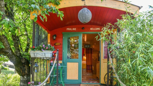 Un bâtiment aux couleurs vives, avec une façade rouge et verte, une enseigne indiquant « BIENVENUE CHEZ PRALINE » et une cloche suspendue à l’entrée.