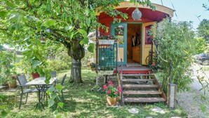 Un petit bâtiment coloré, doté d’un porche, entouré d’une végétation luxuriante et d’un jardin.