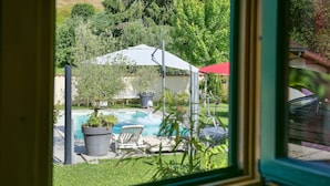 Une vue à travers une fenêtre donnant sur une cour arrière avec une piscine, du mobilier de jardin et un espace couvert.