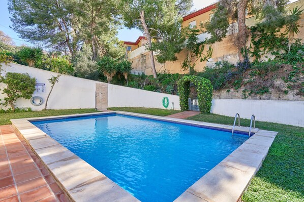 A rectangular swimming pool with clear blue water, surrounded by a tiled deck and a grassy area.