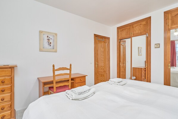 A bedroom with a bed, a wooden dresser, a chair, a desk, and a wardrobe.