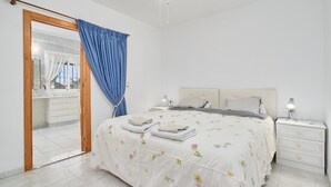 A bedroom with a bed, nightstands, a bedside lamp, a window with curtains, and a view of the bathroom.