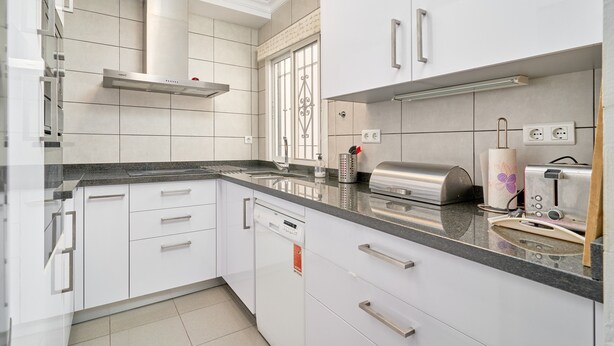 A modern kitchen with white cabinetry, a stainless steel range hood, and a built-in toaster.