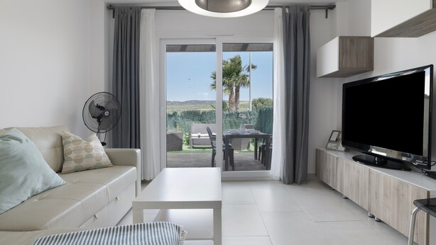 A modern living room with a sofa, a TV, a fan, and a sliding glass door leading to an outdoor patio. - Holiday Home 'Bonita' with Sea Views, Shared Pool and Wi-Fi (ZAHARA DE LOS ATUNES)