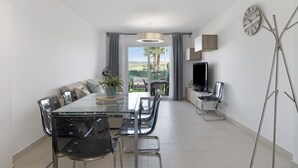 A modern dining area with a glass table, metal chairs, a sofa, a TV, and a view of the outdoors. - Holiday Home 'Bonita' with Sea Views, Shared Pool and Wi-Fi (ZAHARA DE LOS ATUNES)