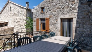 A stone building with a wooden table and chairs, a window with shutters, and a metal railing. - Villa 'Hamlet' with Private Pool, Private Terrace and Wi-Fi (LABLACHÈRE)