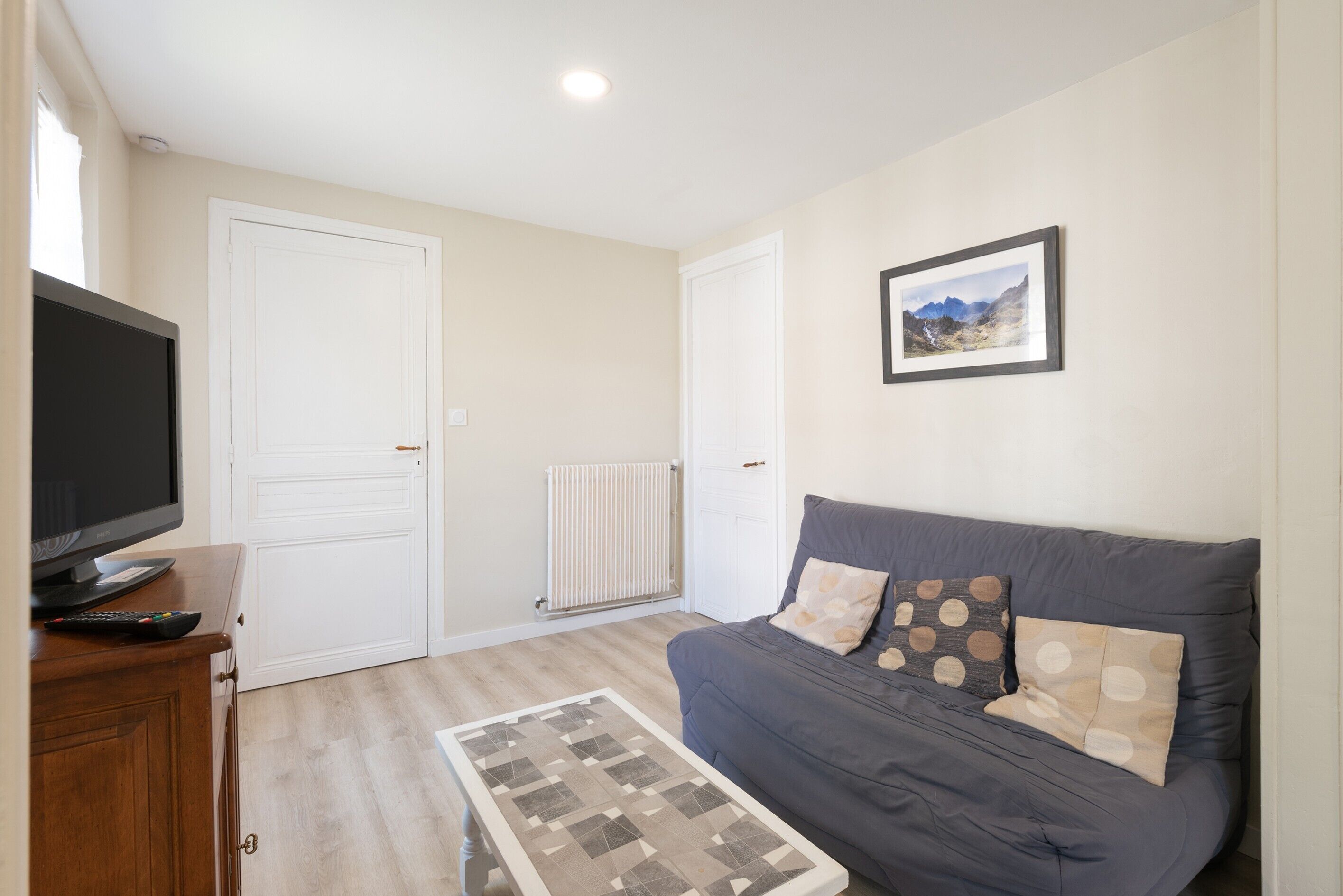 A living room with a sofa, a television, a radiator, and a framed picture on the wall.