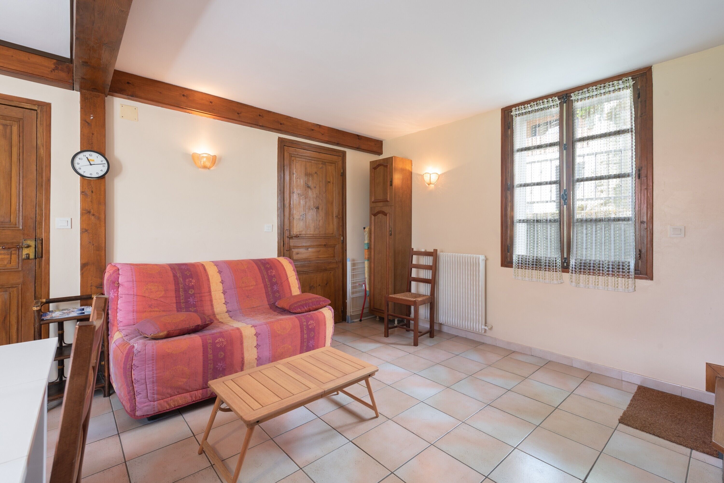 A cozy living room with a wooden ceiling, a sofa, a small table, and a window with blinds.