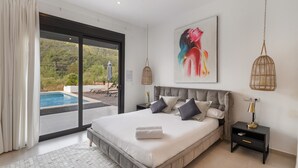 Ein Schlafzimmer mit einem großen Bett, einem Gemälde, einem Nachttisch und Blick auf einen Swimmingpool.