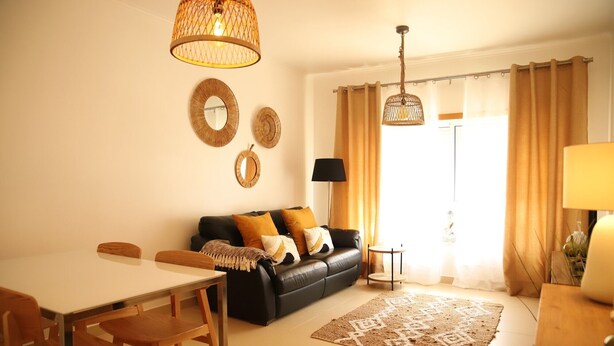 Un salon comprenant un canapé, une table à manger avec des chaises, une lampe et une grande fenêtre avec des rideaux.