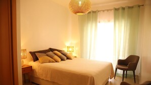 Une chambre à coucher avec un lit, des lampes de chevet, une chaise et une fenêtre avec des rideaux.