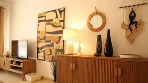 Un salon comprenant un meuble en bois, un téléviseur, une œuvre d’art murale, une lampe et des objets décoratifs.
