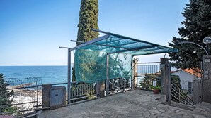 Une terrasse dallée de pierres, dotée d’une véranda en verre, d’un portail en métal et offrant une vue sur la mer.