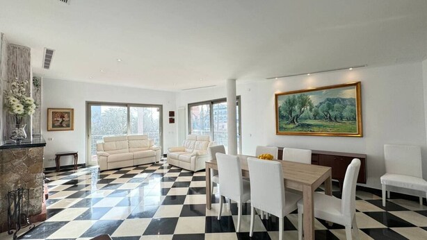 Un salón amplio con piso a cuadros, dos sofás, una mesa de comedor con sillas y un cuadro grande en la pared.
