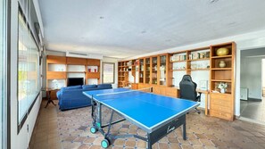 Et værelse med et ping pong bord, en sofa, et skrivebord og en bogreol.