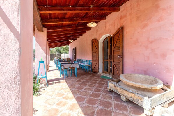 A covered patio area with a tiled floor, wooden furniture, and a stone basin.