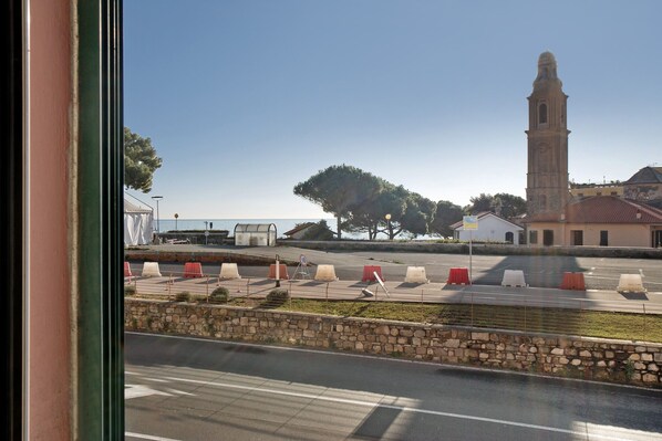 Vista de una calle con un muro de piedra, una carretera con líneas blancas y un edificio con una torre.