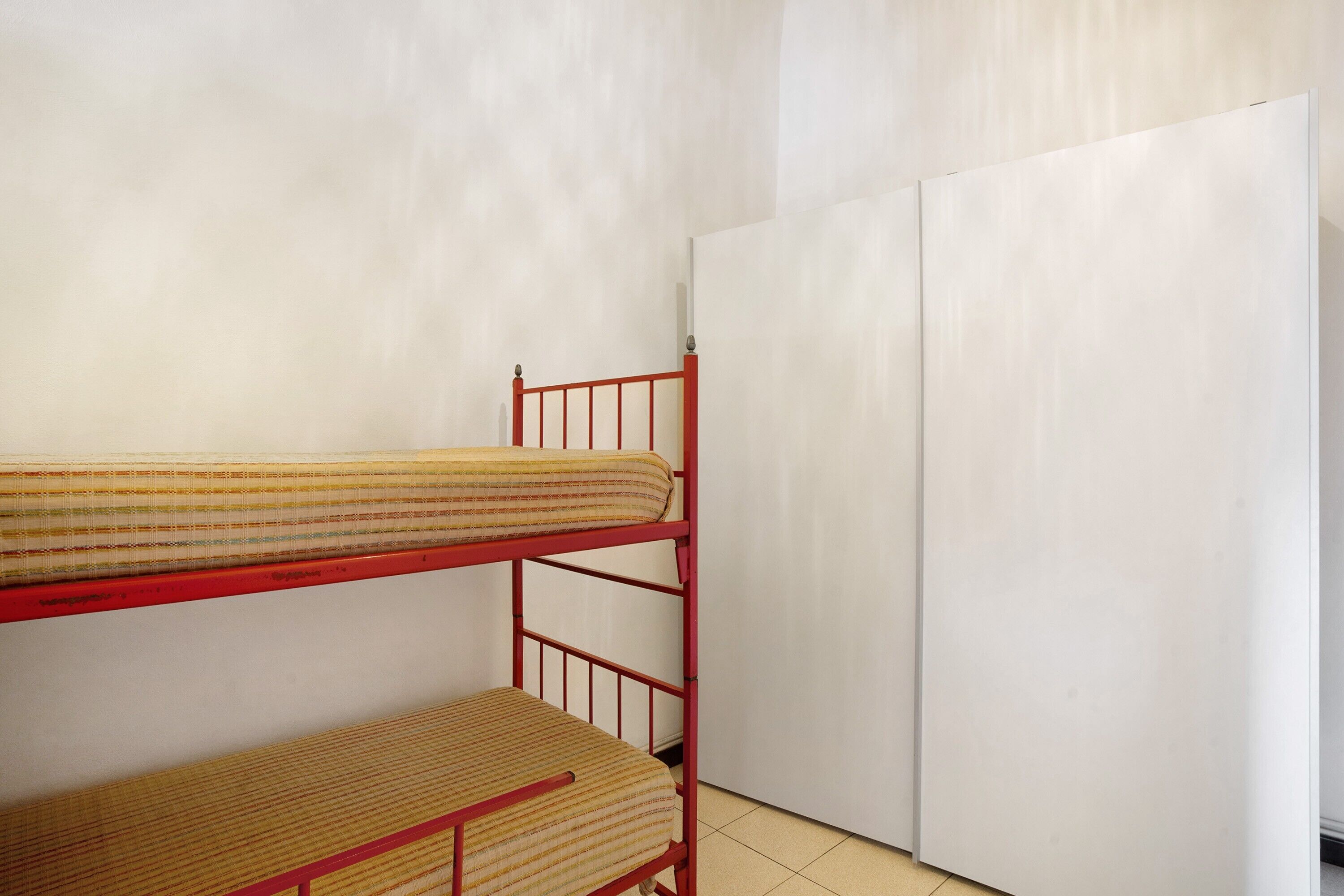 Een stapelbed met een rood frame en een witte kledingkast in een kamer met effen muren.