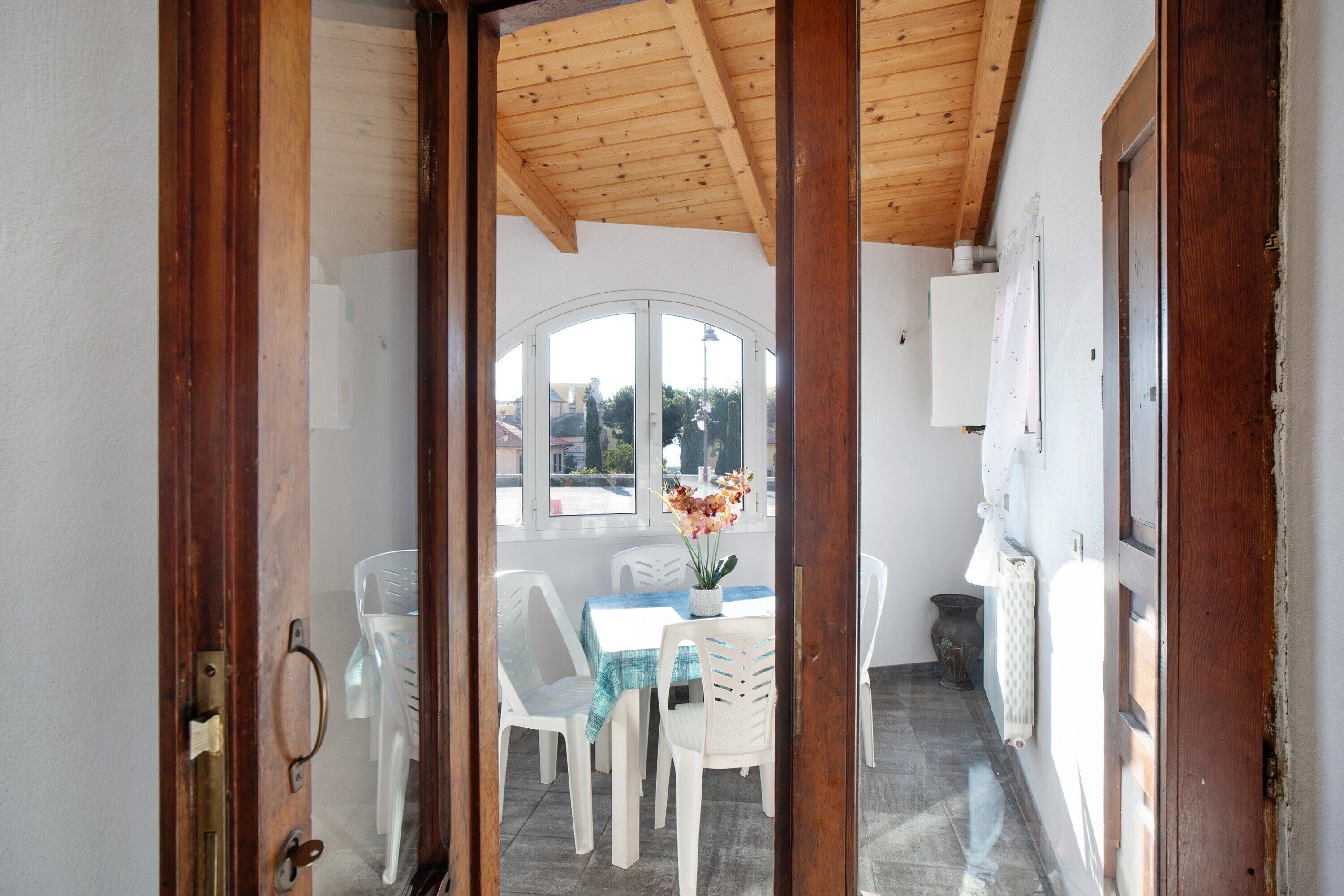 An open wooden door leading to a dining area with a table and chairs, a potted plant, and a view of the outside.