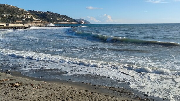 Una playa con olas, cielo despejado y un paisaje montañoso distante.