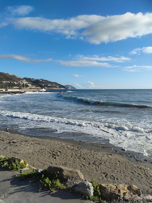 Una playa con olas, cielo despejado y un paisaje montañoso distante.