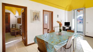 Un comedor con una mesa, sillas, un florero con flores, un televisor y vistas al exterior.