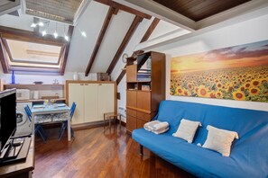 Une pièce avec un canapé bleu, des meubles en bois, une lucarne, un tableau représentant des tournesols et un lave-linge.
