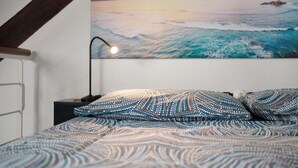 A bedroom with a bed, a nightstand, a lamp, and a wall painting of a seascape. - Apartment 'Lovely Loft' with Wi-Fi and Air Conditioning (Sanremo)