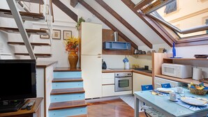 A compact kitchen with a wooden staircase, a dining area with a table set for two, and a TV in the corner. - Apartment 'Lovely Loft' with Wi-Fi and Air Conditioning (Sanremo)