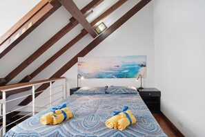 Une chambre à coucher comprenant un lit, une table de chevet, un tableau représentant un paysage marin et une structure de plafond en bois.