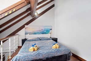 A bedroom with a bed, a painting, and a staircase.