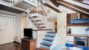 A room with a wooden staircase, a dining table with plates and cups, a kitchen area with a stove, and a TV on a cabinet. - Apartment 'Lovely Loft' with Wi-Fi and Air Conditioning (Sanremo)