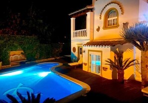 A swimming pool with a curved design, a white building with a balcony, and a palm tree. - Villa 'Alba' with Private Pool, Wi-Fi and Air Conditioning (Santa Eulària des Riu)