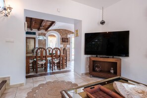 A living room with a TV, wooden furniture, a stone wall, and a dining area with chairs and a table. - Villa 'Alba' with Private Pool, Wi-Fi and Air Conditioning (Santa Eulària des Riu)