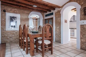 A dining area with a wooden table and chairs, stone walls, and a view into the kitchen. - Villa 'Alba' with Private Pool, Wi-Fi and Air Conditioning (Santa Eulària des Riu)
