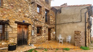 Un bâtiment en pierre doté d’une cour, d’une porte et de deux chaises en métal blanc.