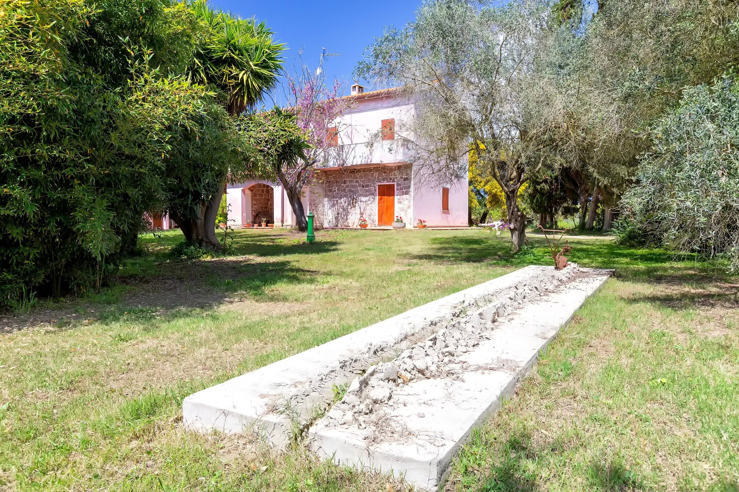 A stone building with a red door, surrounded by trees and a grassy area.