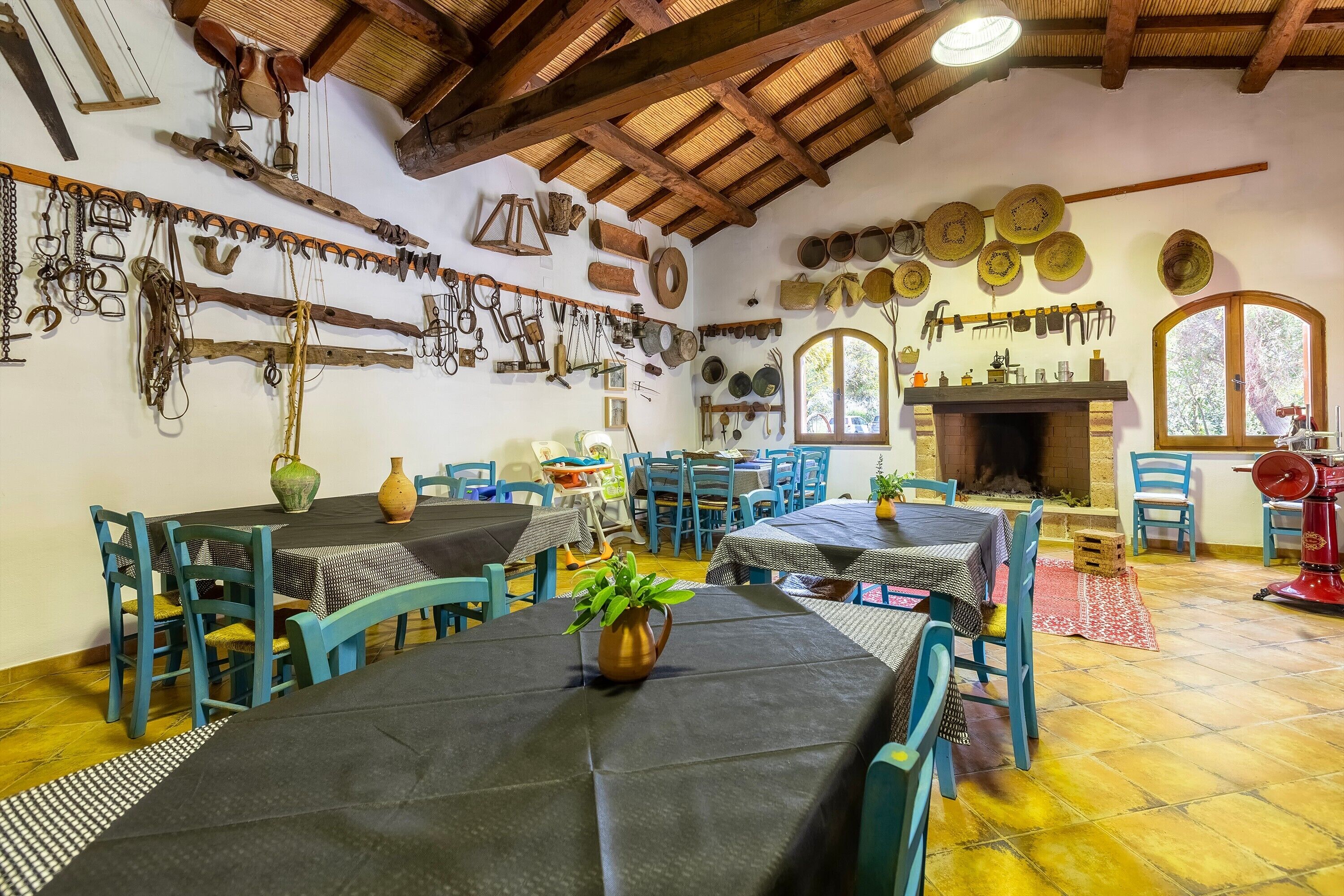 Un coin repas rustique avec des tables et des chaises en bois, une cheminée, ainsi que divers ustensiles de cuisine et ustensiles de cuisson accrochés aux murs.
