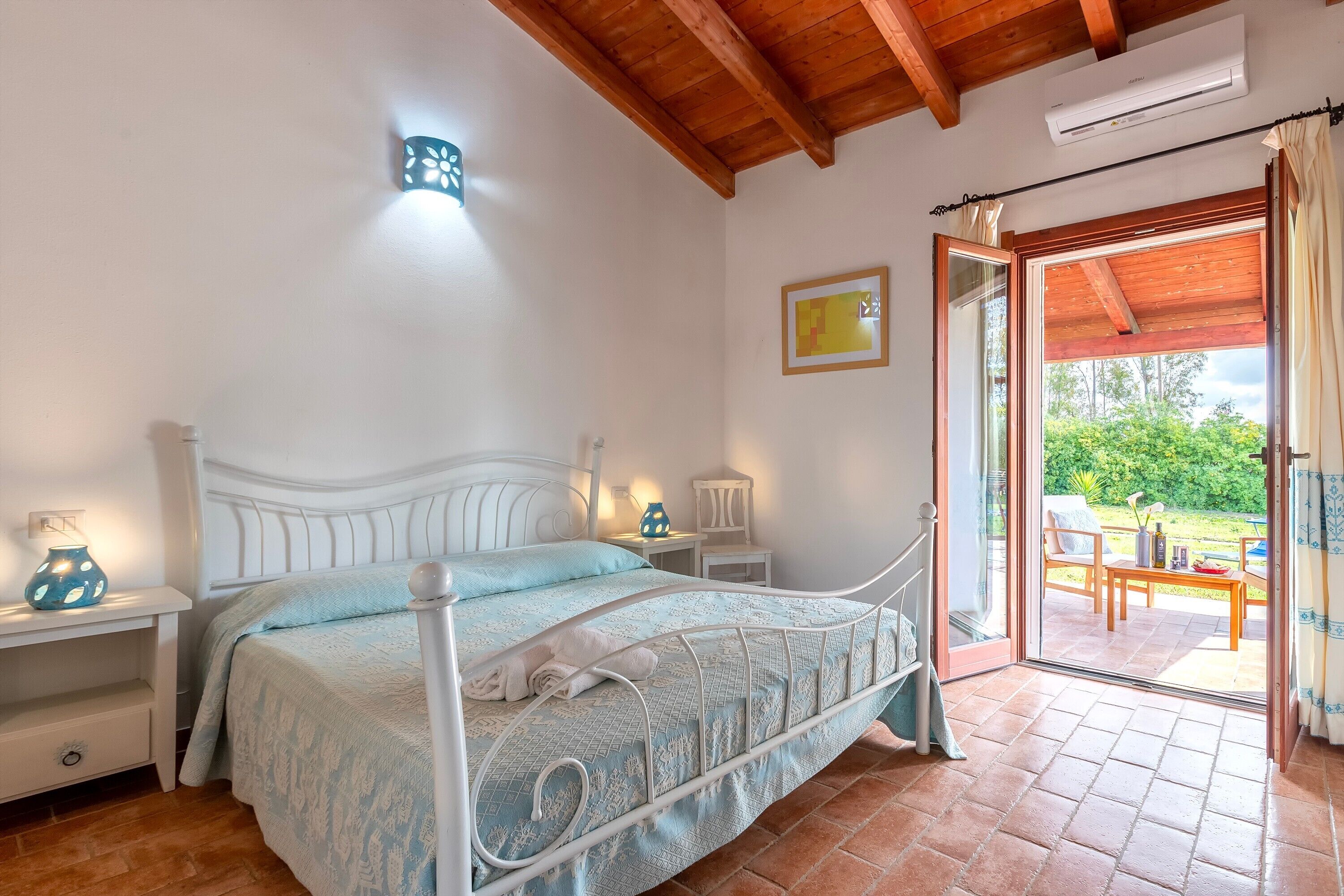 Une chambre à coucher comprenant un lit, des tables de chevet, une commode, un appareil de climatisation, une fenêtre et une porte ouverte donnant sur un patio extérieur.