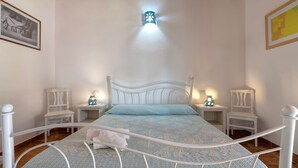 Un dormitorio con cama, cabecero blanco, mesitas de noche y una mesilla.