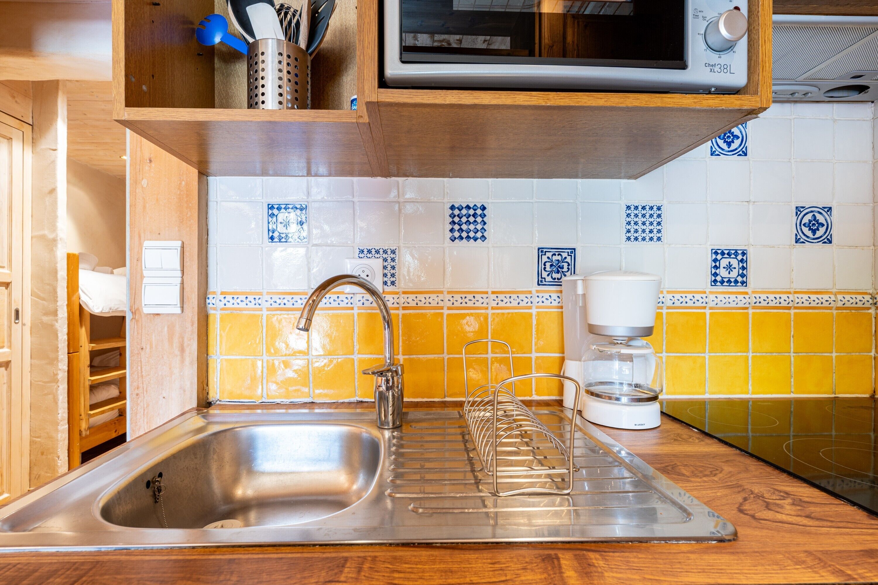 Una cocina con un lavamanos de acero inoxidable, una cafetera y un microondas encima.